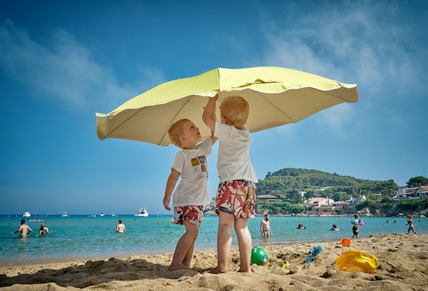 Two children on the beach playing with a yellow parasol