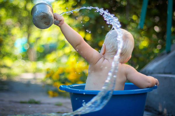 Blonde toddler sat in blue buckets playing with water