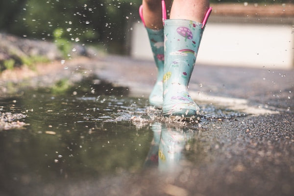 Child in blue patterned wellington boots splashing through a puddle