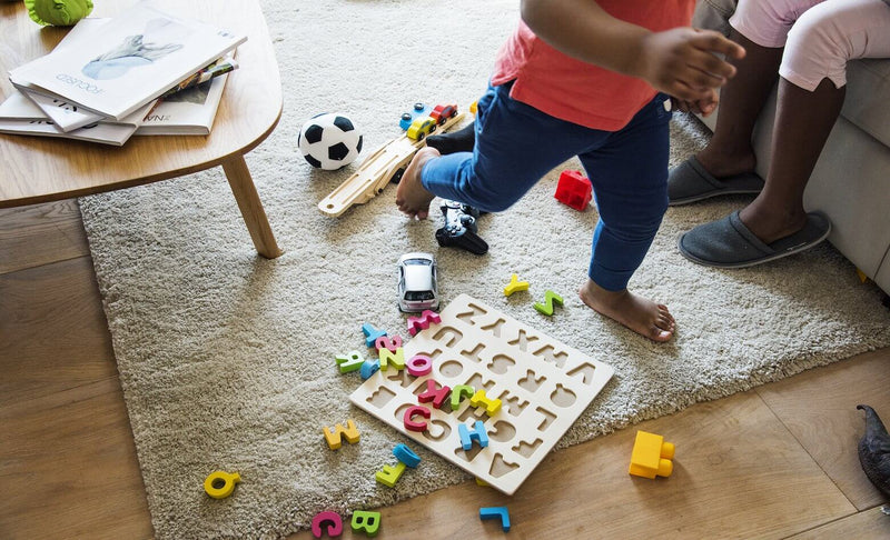 Child running around inside over wooden letters on a rug